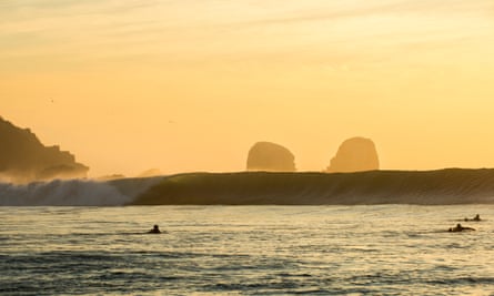 Surfers in the ocean at sunset, Pichilemu, Chile.