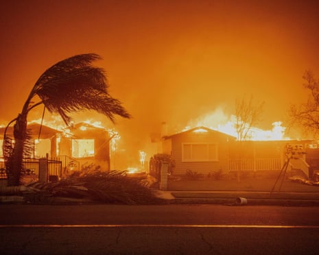 Houses engulfed in flames with a palm tree bending in strong winds and smoke filling the air