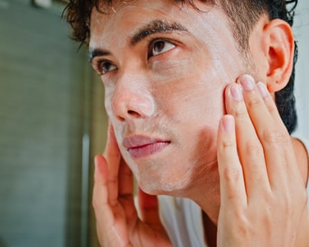 Young man washing his face with a facial cleanser in front of mirror in bathroom at home