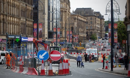 Roadworks, cones, fencing and a no-entry sign in a closed street in the city centre, with a view down the street showing shops and historic stone buildings