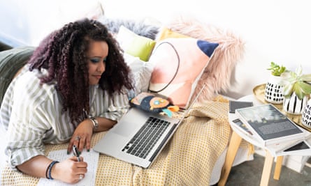 A woman lies on a bed working on her laptop