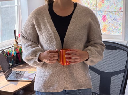 a woman holding a mug while wearing a cardigan by desk in office