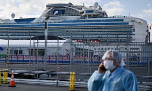 A man in protective gear speaks on the phone near the Diamond Princess cruise ship