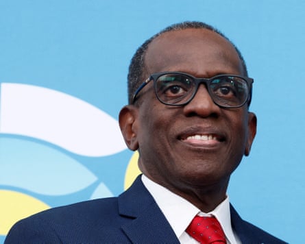 Headshot of Philip Pierre in a blues suit and red tie in front of a pale blue background with part of a logo