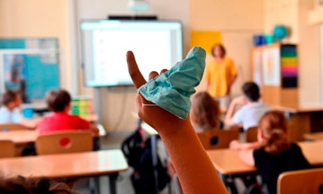 A facemask is seen on the hand of a student raising his arm during class.