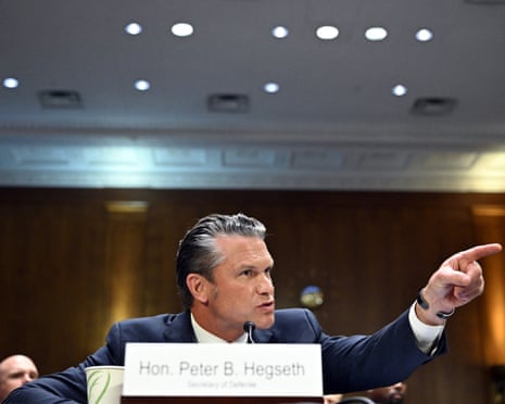 Pete Hegseth speaks into a microphone while pointing during a Senate hearing.
