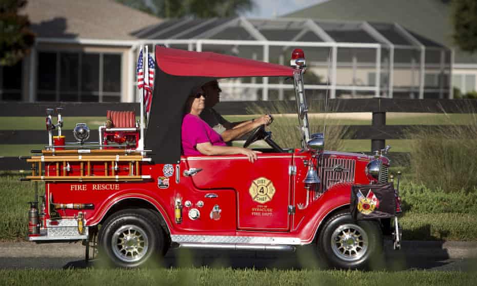 A couple drive a golf cart converted to look like a fire truck in The Villages retirement community.