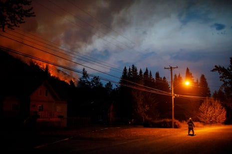 A firefighter walks under a streetlight as the Embleton Mountain wildfire rips down the mountain towards the edge of the village of Whitecroft, B.C.