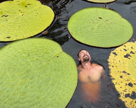 A man floats among giant waterlilies, his eyes closed and smiling