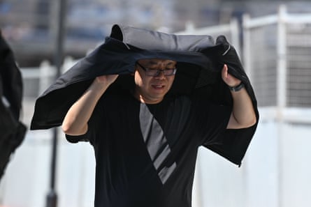 A man hold his jacket over his head as shade as he walks along the street