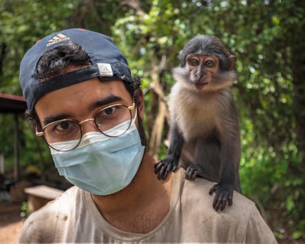 A man in a baseball cap and a blue mask with a small monkey on his left shoulder.