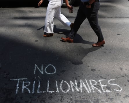 ‘No trillionaires’ written in chalk on a sidewalk as two people walk by