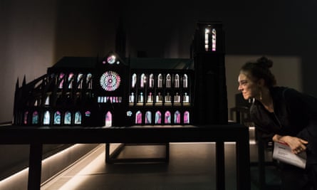 a woman looking into an illuminated model of notre dame in a dark room