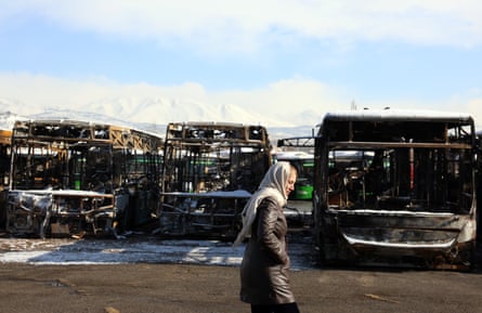 A woman wearing a headscarf walks past three burnt-out buses