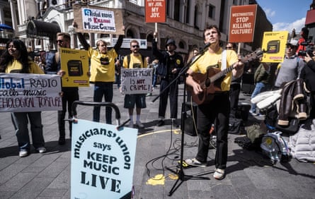 A man plays the guitar while other protesters hold placards behind him