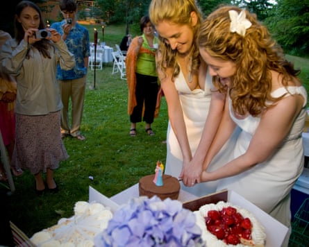 A couple cutting their wedding cake at their lesbian wedding reception with guests looking on
