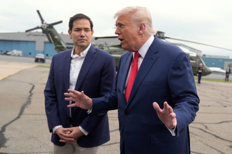 A man with dark hair and a blue jacket stands next to a man with orange hair and a blue jacket.