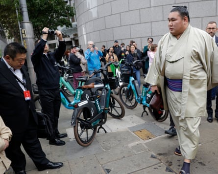 Grand champion Hōshōryū Tomokatsu walks from his hotel, surrounded by people taking photos.