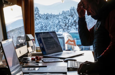 Mark Diggins sitting at a desktop computer with a view of the Cairngorms through his window