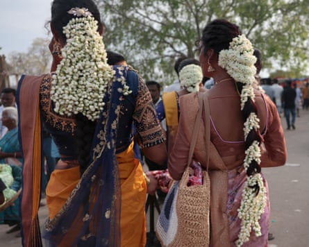 Two women, seen from behind, with intricate jasmine garlands wound into their hair and wearing silk saris
