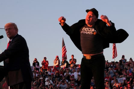 Elon Musk jumps awkwardly behind Donald Trump on stage.