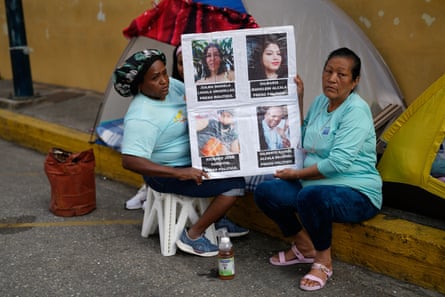 two women hold up a placard of photos of their loved ones in detention