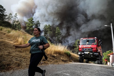 A woman runs as a fire appliance and thick smoke plumes approach