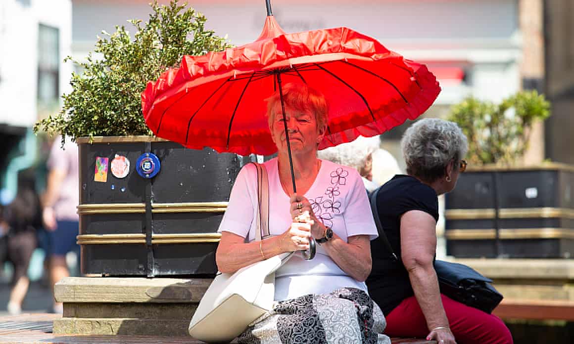 A woman sits on a bench with a large red umbrella.