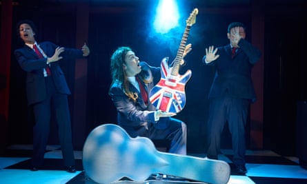 Charlie Baker as Blair holds up a union-jack guitar in Tony! (The Tony Blair Rock Opera)