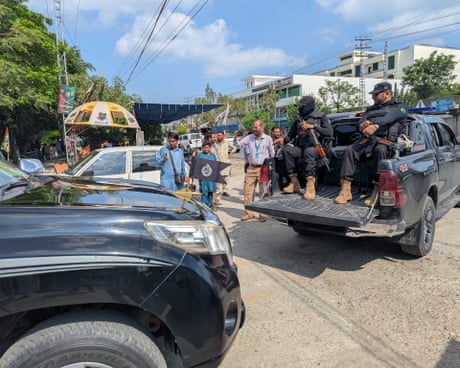 Two armed uniformed men in back of pickup on street with several other people and cars in shot Two armed uniformed men in back of pickup on street with several other people and cars in shot