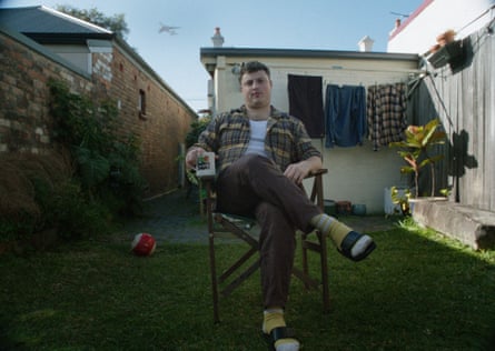 A young man sitting in a deck chair in his backyard, holding a mug