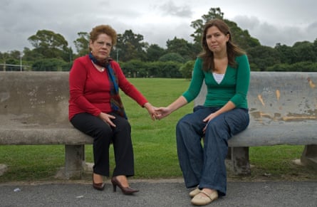 An older woman holding hands with a young woman while they are sitting on park benches