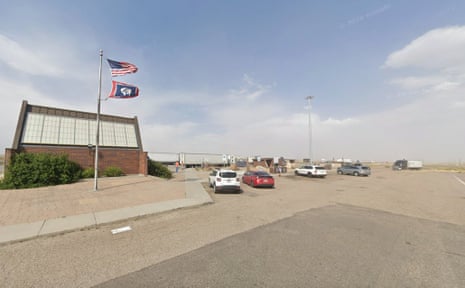 Parked cars at a rest area near a brick building with flags flying overhead