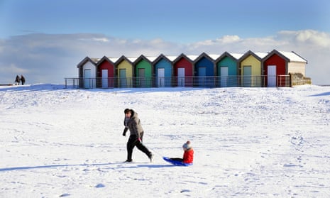 A woman pulls a child on a sledge through the snow beside beach huts in Blyth, Northumberland.