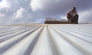 A solar panel technician carrying out maintenance work on a corrugated roof, Miono region, Tanzania.