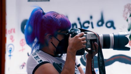 A woman with her hair in a ponytail holds a professional camera to her eye.