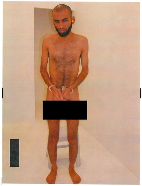 man stands handcuffed and naked in a brightly lit white room. a black bar covers his groin qhiqqhiqxihqinv