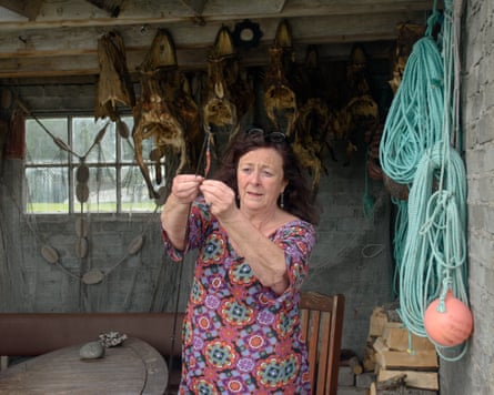 A woman in bright dress putting bait on the end of a fishing hook in a hut with what look like skulls of large fish hanging from the ceiling
