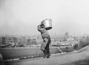 black and white photo of back view of man carrying a bucket outside while walking