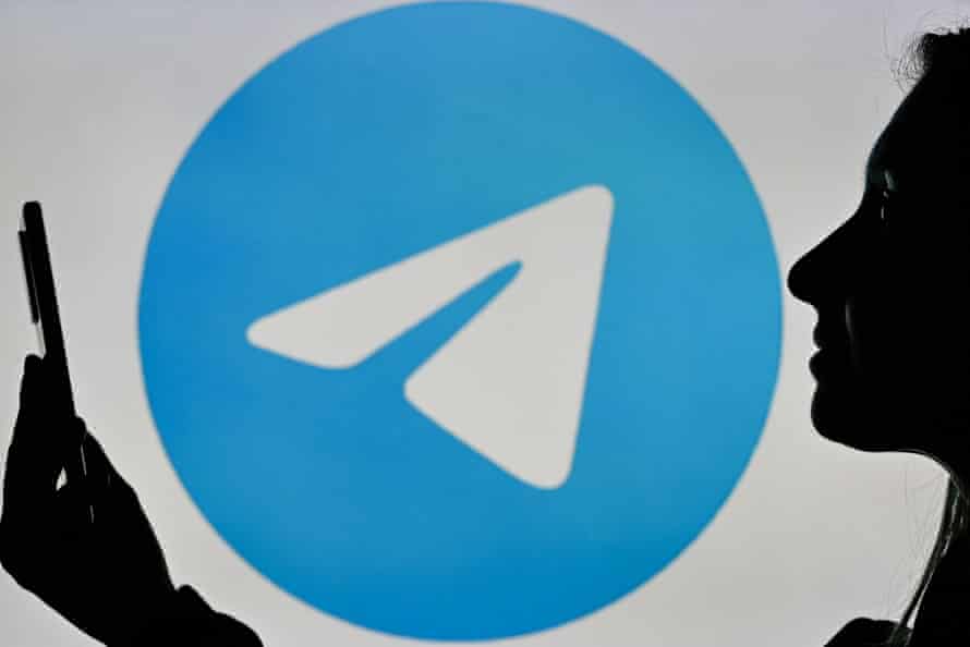 A woman holding a cell phone in front of a Telegram Messenger logo