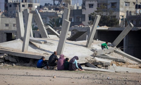 A Palestinian family sit next to a destroyed house in al-Nuseirat refugee camp.