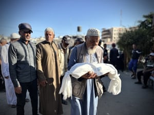 A man carries the body of an infant wrapped in a shroud