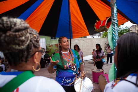 A black women with braids holds a percussion drum at the centre of a group of other women