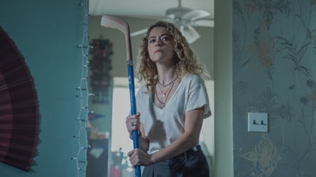 A woman with curly hair holds an ice-hockey stick.