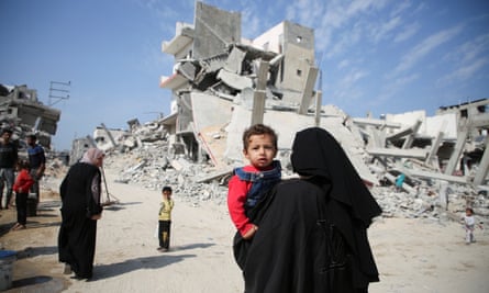 A Palestinian woman carries a child as they walk past the rubble of houses destroyed by the Israeli military in Khan Younis in the Gaza Strip, on 6 November 2024.
