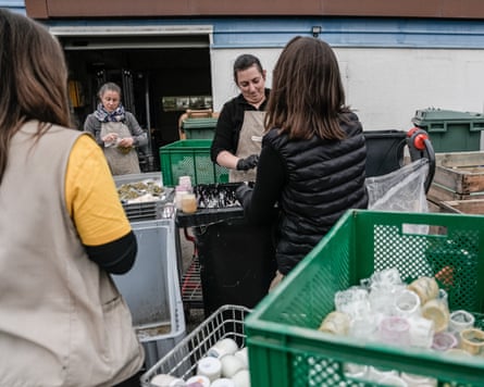Supermarket employees sort jars and crates of food in bins and crates outside