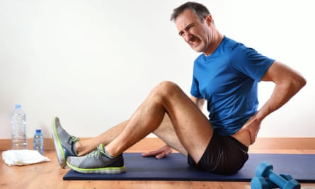 Man working out indoors winces as he holds his lower back.