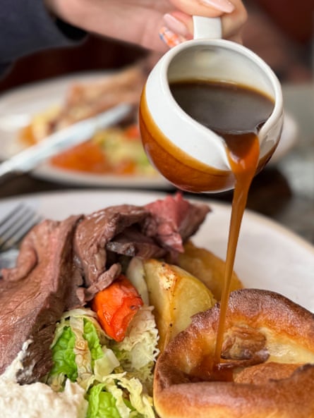 Gravy being poured over traditional roast beef with roast potatoes, yorkshire pudding and vegetables.
