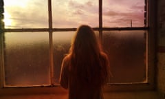 Rear view of a woman looking out of the window at sunset.