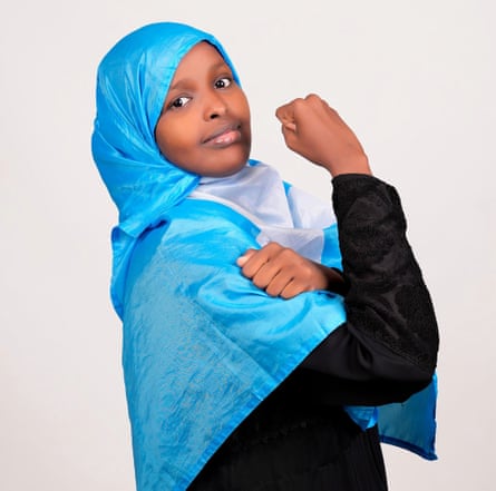 Portrait of Sadia Moalim Ali wearing a blue headscarf and raising her arm in a fist